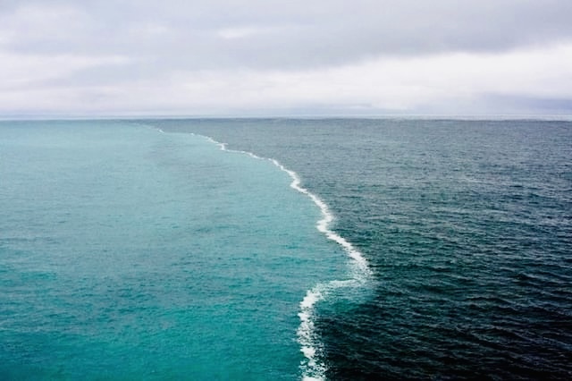 The meeting of the Atlantic and Pacific, two distinct bodies of water visibly touching, turbulent at the border, maintaining their separate character on either side.